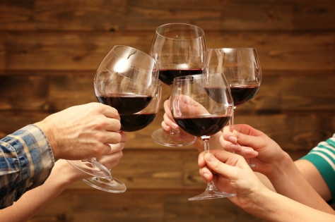 Clinking glasses of red wine in hands on rustic wooden planks ba